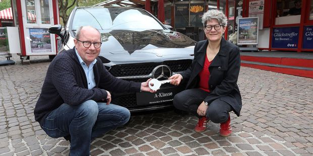 Vor den rot weißen Losbuden steht der schwarze Mercedes, davor hocken links Dietmar Hoppe von der  Bürgerpark-Tombola, rechts Simone Schnase, die Gewinnerin des Mercedes. Symbolisch halten beide einen großen Schlüssel in der Hand. Das Foto wurde von Martin Rospek gemacht.